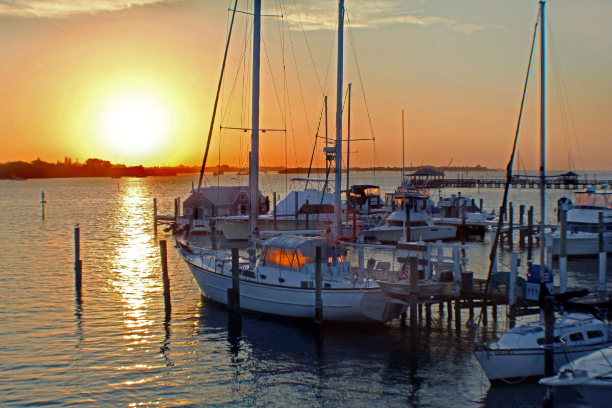 Sailboats and motorboats docked at a marina during a golden sunset.